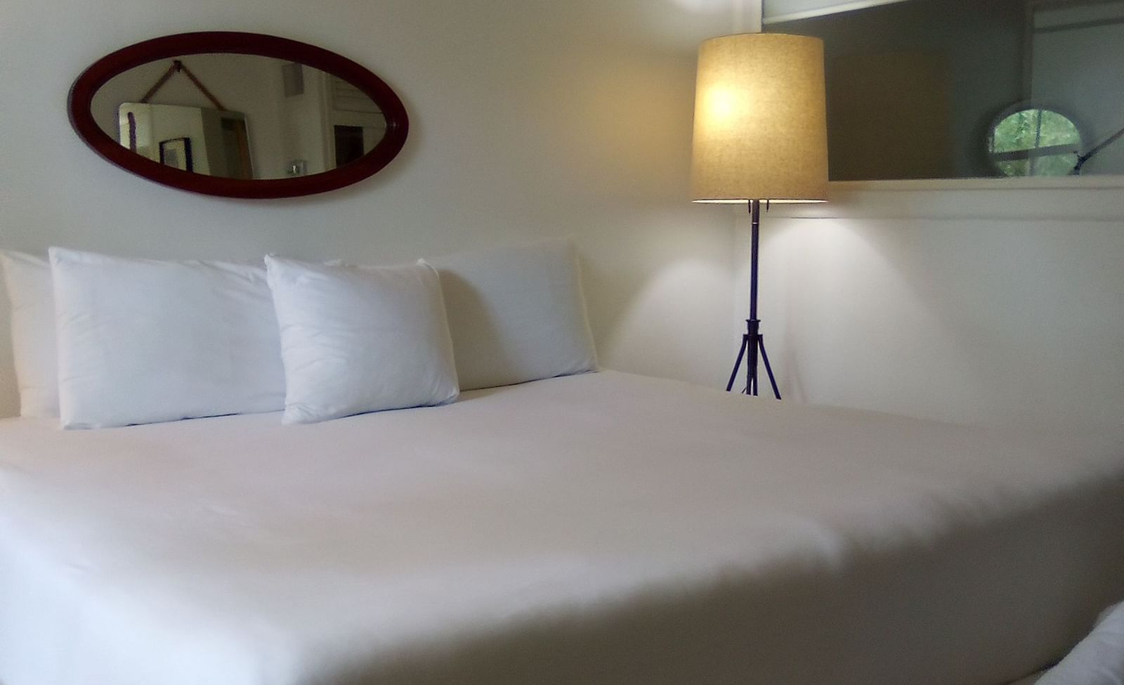 A single bed at Casa Morada with white bedding, a floor lamp, and an oval mirror mounted on the wall above the headboard.