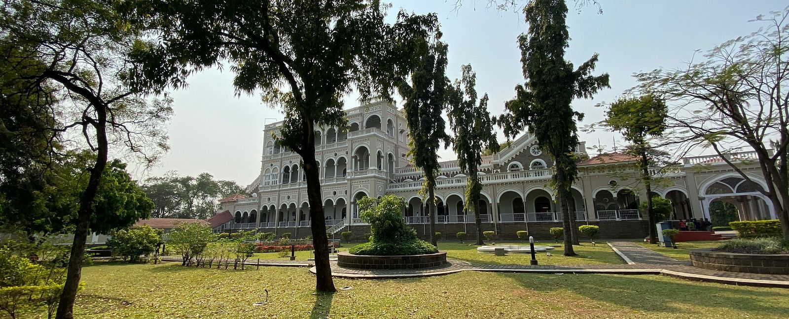 An overview of Aga Khan Palace with trees and a manicured garden in front of it.