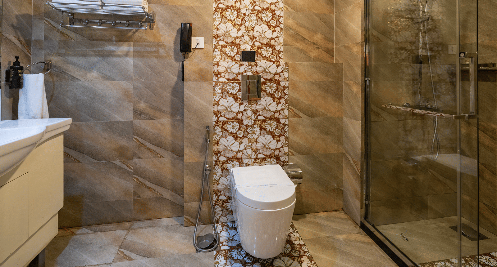 The bathroom in the Honey Moon Suite at Parakkat Nature Hotel and Resorts, Munnar, featuring textured wall tiling, a sink vanity, a toilet, and a glass-enclosed shower.