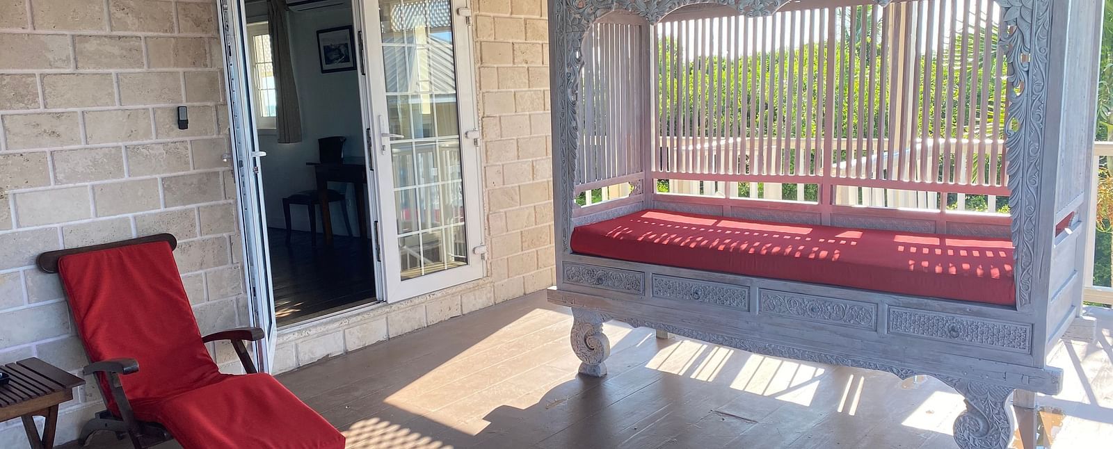 Veranda with red lounge chairs and sunlight streaming through white railing | A Stone's Throw Away
