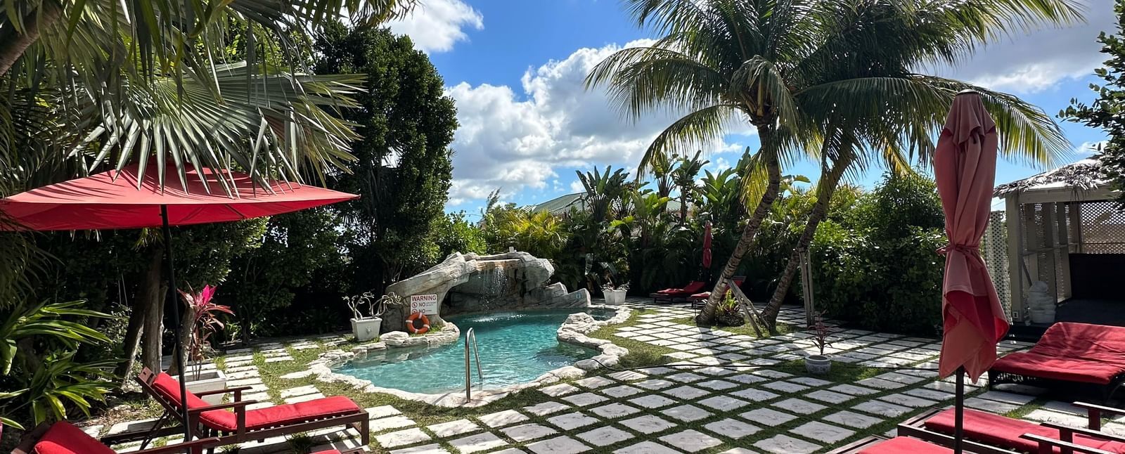 Poolside seating with red lounge chairs and umbrellas surrounded by palm trees | A Stone's Throw Away
