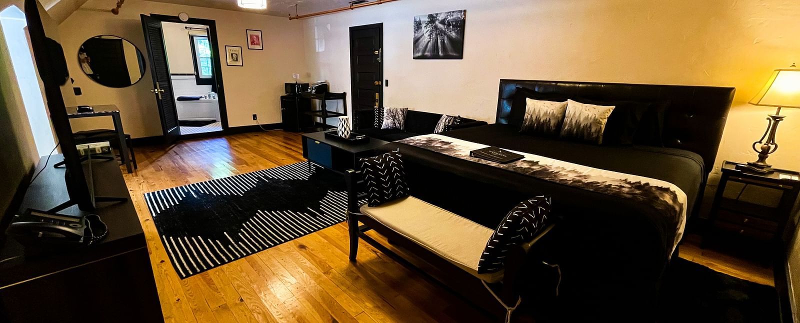 corner view of a room featuring a double bed along with a common seating are in the far end highlighting the black furnishings and decor - Historic Tapoco Lodge