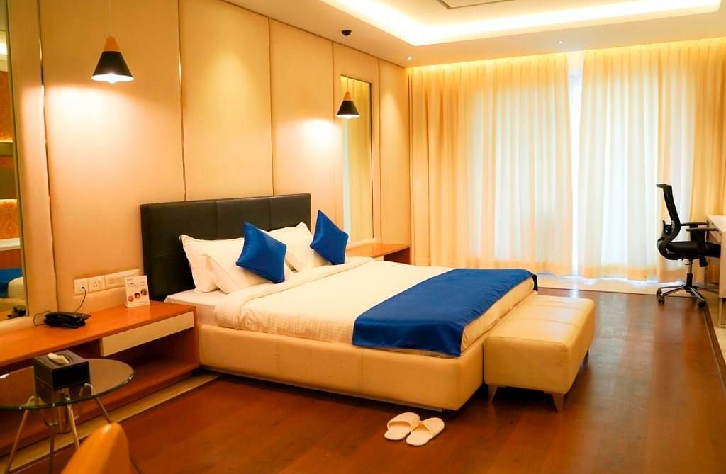 A warm and inviting hotel room at BNGV Grandeur Hotel and Banquets, featuring a bed with blue linens, wooden accents, and soft ambient lighting.