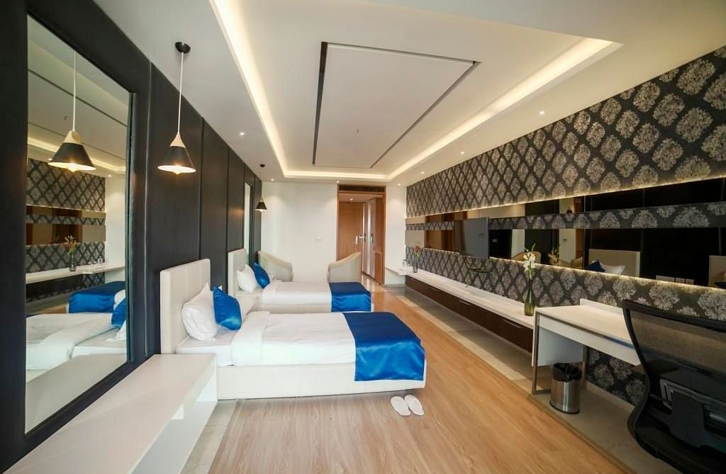  spacious hotel room at BNGV Grandeur Hotel and Banquets, with a long perspective showcasing the bed, a desk area, and modern architectural lines.