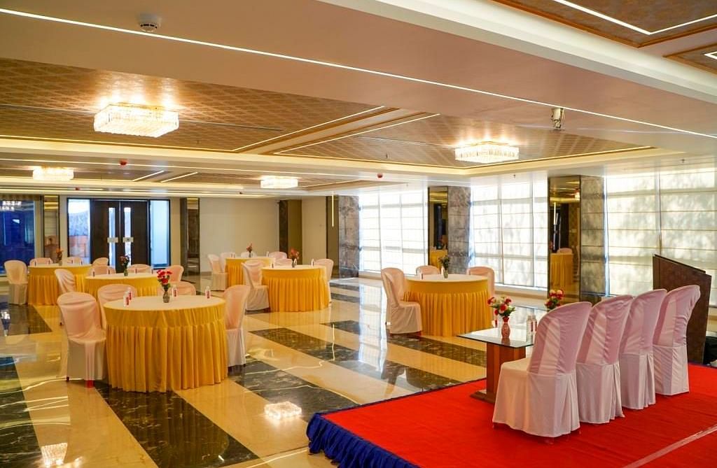 A grand banquet hall with round tables, a red stage, and white chairs, ready for an event, featuring ornate ceilings.
