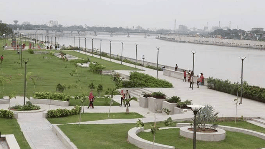 An upper view of the Sabarmati Riverfront, showcasing lush grass areas and walking paths along the river, where people are leisurely enjoying the surroundings.