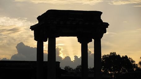 An overview of ancient columns in Belur with the sun's rays behind the clouds in the background.