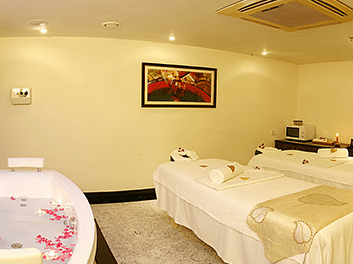 Well-lit spa room with two massage beds and a tub decorated with flower petals.