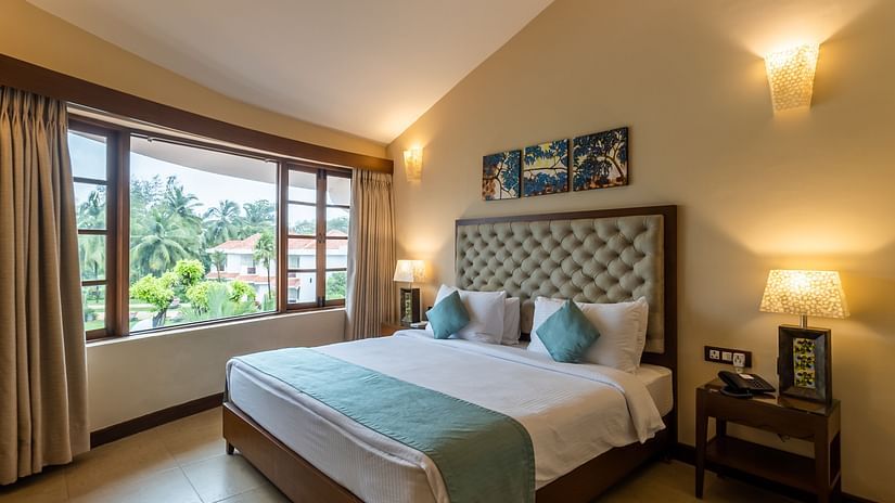 An overview of a suite with a cosy king size bed and mellow lighting at Heritage Village Resorts and spa, goa.