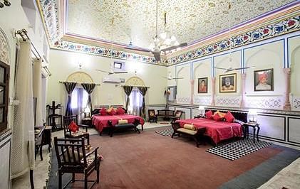 A large suite at The Umaid Vilas Jaipur with two beds dressed in red linens, a patterned ceiling, and traditional Indian decor.