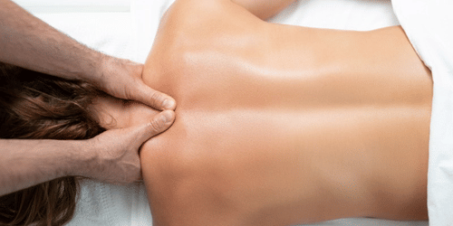 A person lying on their stomach with bare back, receiving massage on the back of their neck