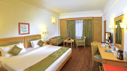 An overview of the Suite at Abad Atrium, MG Road, with a double bed, table tables and lamps in view at one of the best Hotels near Broadway, Kochi.