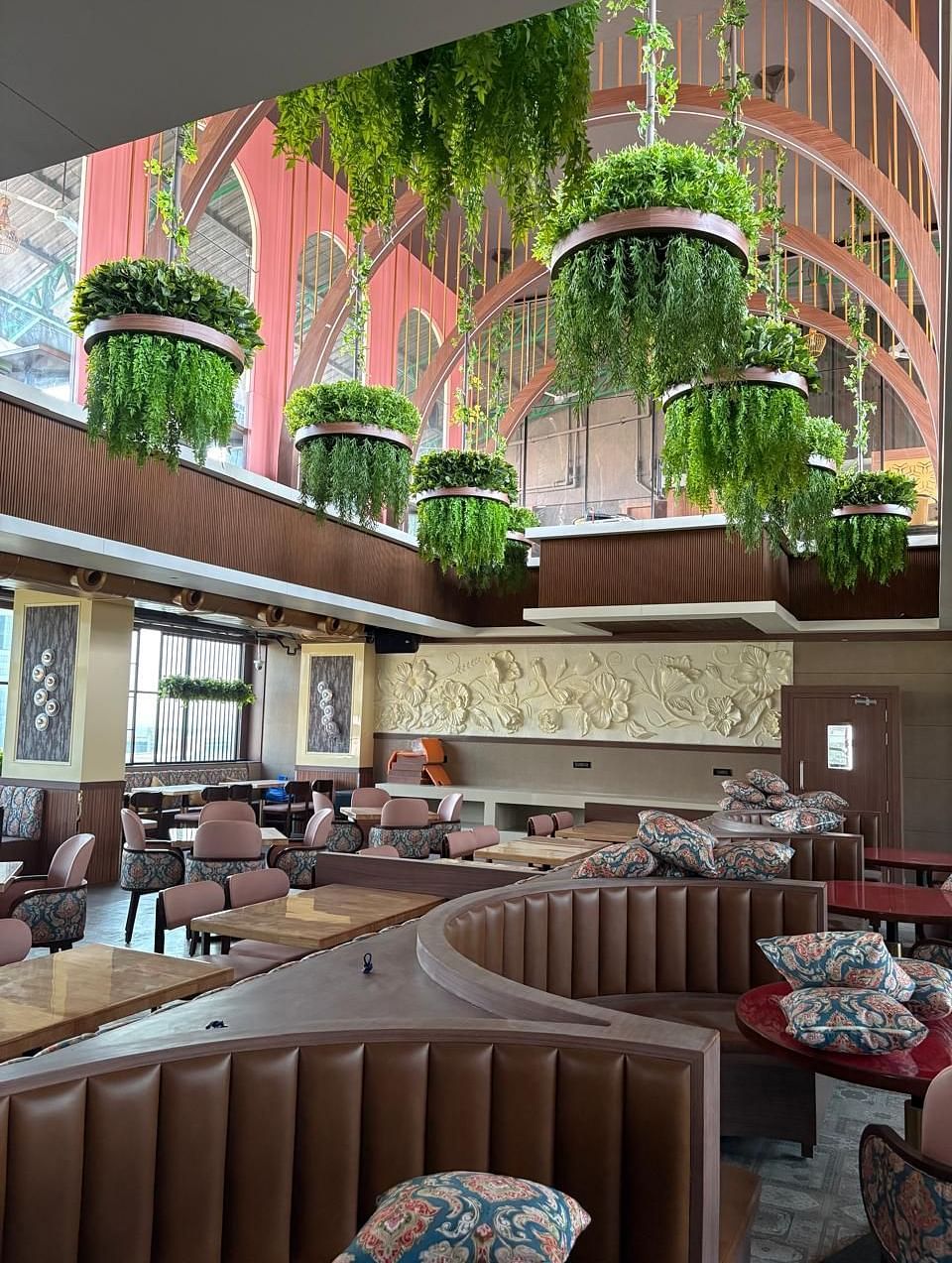 A warmly lit restaurant area with booth seating, wooden tables, and hanging plants as part of the decor - Melior Inn
