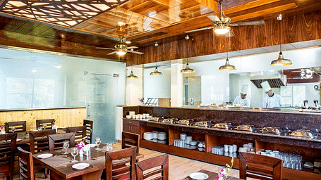 The restaurant at Regenta Inn DLS featuring the kitchen separated by a glass partition with a buffet counter in front of it.