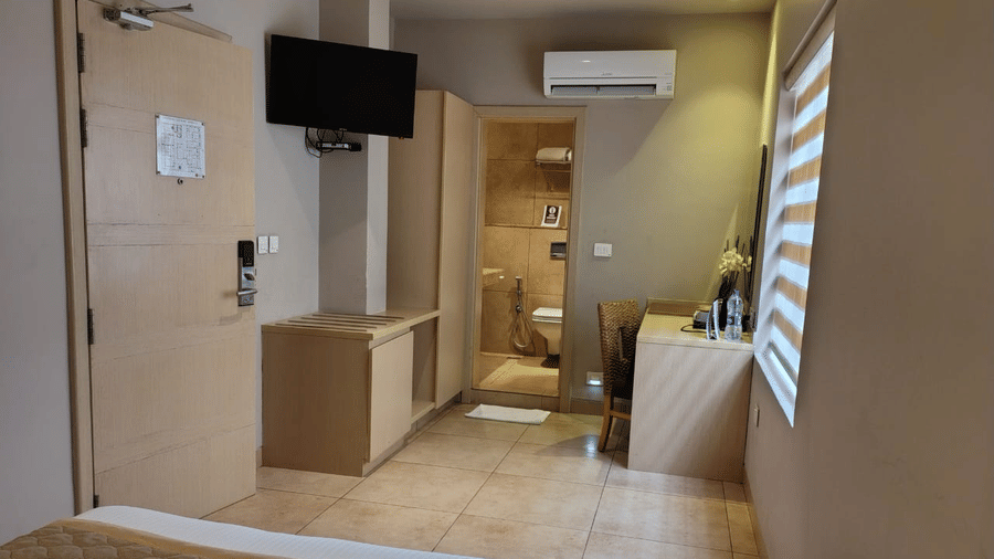 Interiors of the Lawn View Room at Cholaa Dynasty, Kumbakonam featuring a bed, flat TV screen, AC, cabinet tables, and a workstation.