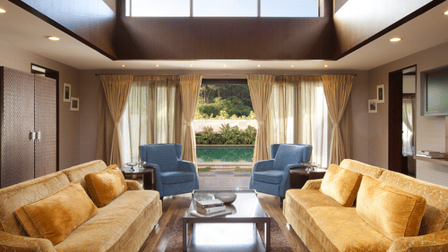 Seating area in living room of The Residence at The Serai Chikmagalur, highlighting the upholstered sofas, glass centre table, large glass windows offering views of the outdoors.