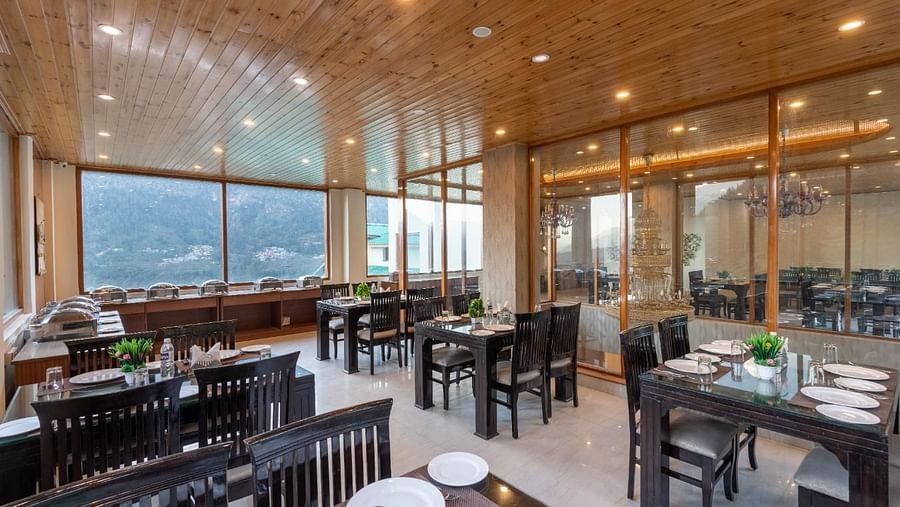 The image showcases a contemporary restaurant with large windows framing stunning mountain views  | DLS Serenity Resort and Spa