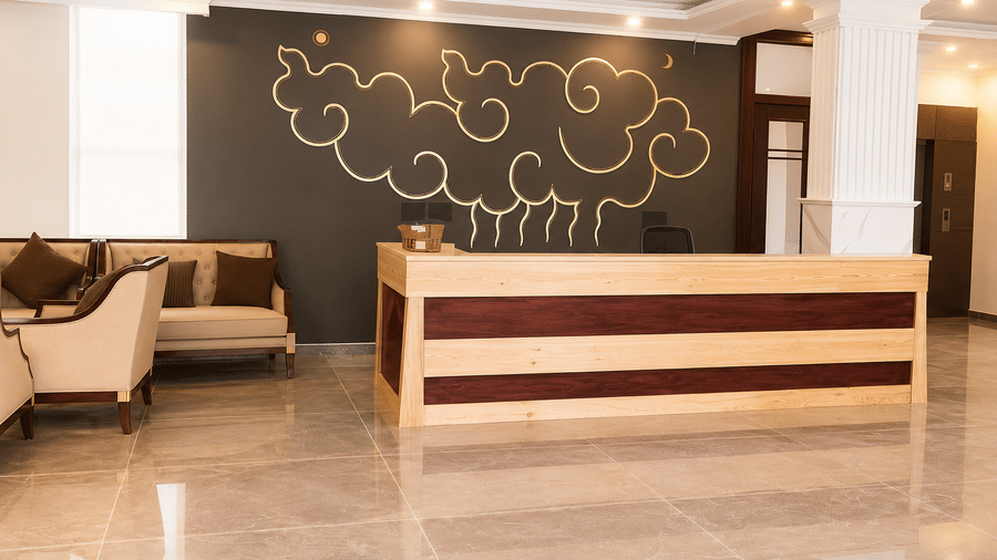 Hotel lobby reception desk with a wooden and maroon counter, patterned wall art behind, seating nearby and polished marble flooring below.