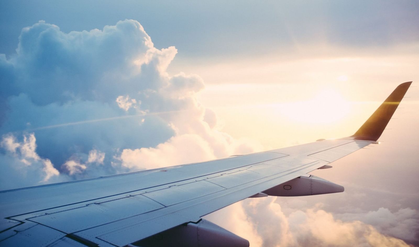 An aircraft wing slices through sunlit skies above cottony clouds.