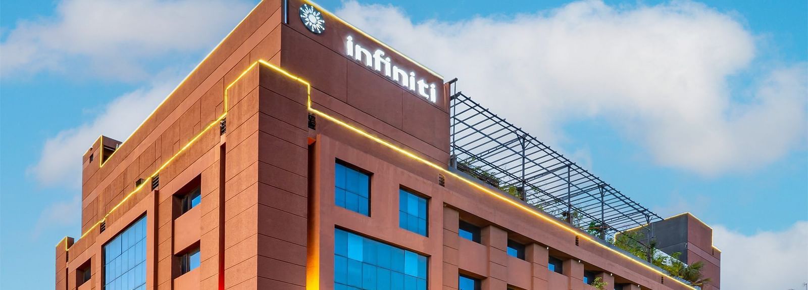 Exterior view of a multi-storey Infiniti Hotel, Indore with large glass windows, landscaped greenery, and visible signage on the top.
