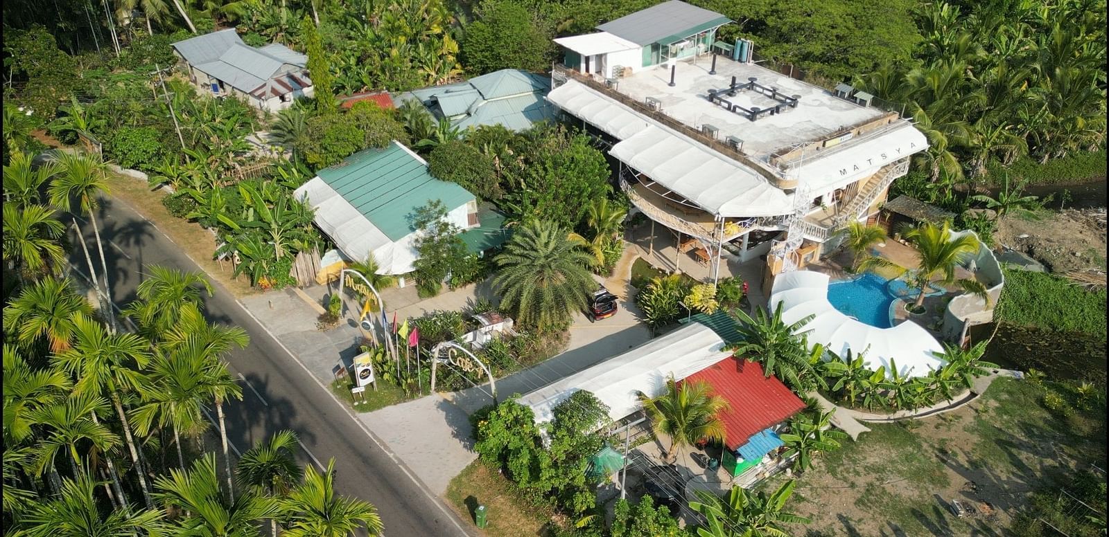 An aerial view of Matsya Island Retreat by Island Quest, showing buildings, a pool, and lush greenery.