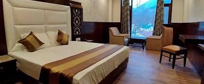 A spacious hotel room with a king size bed, two armchairs, a coffee table, a desk, and a window overlooking a garden | DLS La Serene Manali