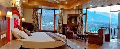 A spacious and luxurious hotel room with a round bed, plush seating, a balcony overlooking a scenic view, and elegant decor | DLS La Serene Manali
