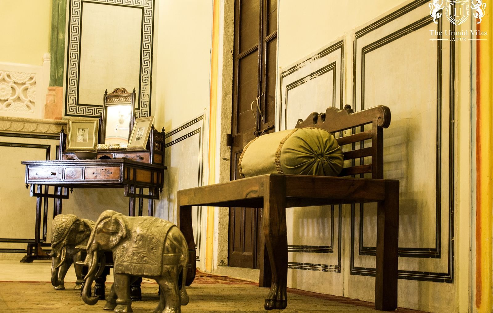 A room at Umaid Vilas Jaipur with a wooden bench, elephant sculptures, and a desk with a mirror.