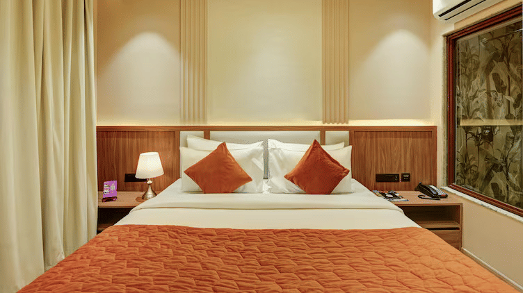 Front view of the double bed at the Standard Room with a crimson bed runner spread over it along with cushions at Hotel 91 Privé, Gurugram.