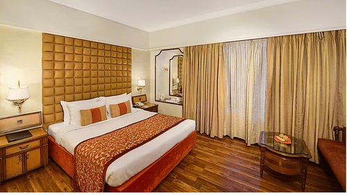 Deluxe King Room at Pride Premier Pune featuring a plush bed and a couple of nightstands on both sides with lamps above them