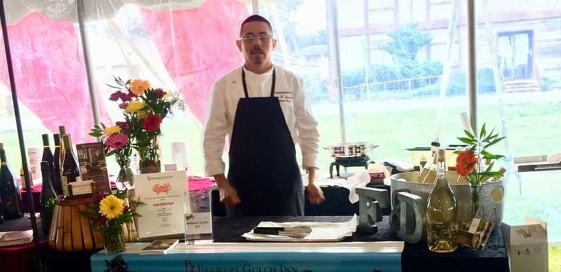 A chef standing behind a decorated table at an outdoor event under a tent.