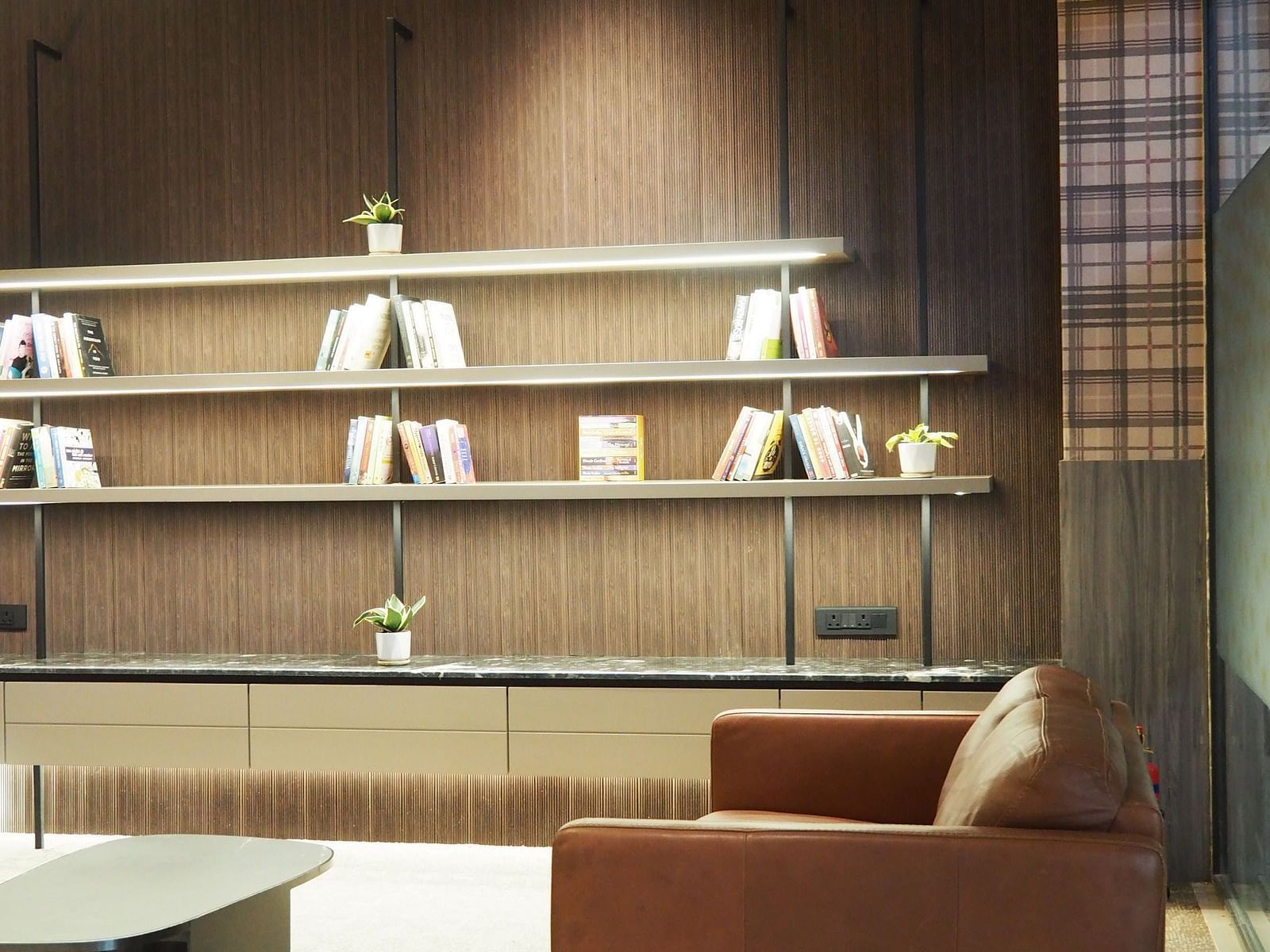 A modern room with two armchairs, a small table, and open shelves on a dark wall - Club Charholi, Pune 