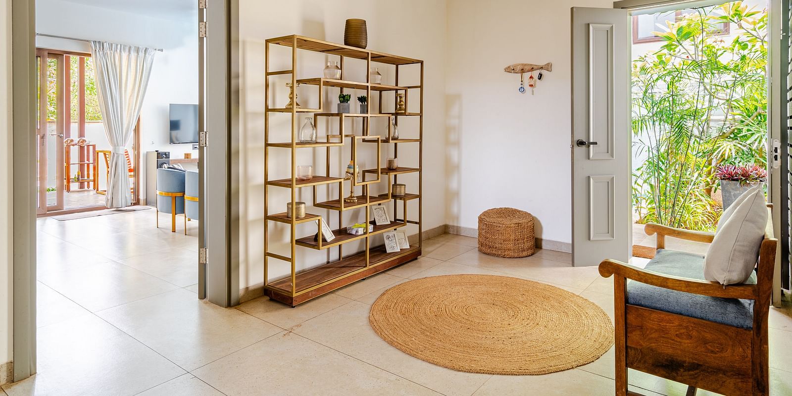 Bright and airy hallway with an open door leading to a garden, decorative bookshelf, circular jute rug, and a wooden armchair - Lindsay Manor