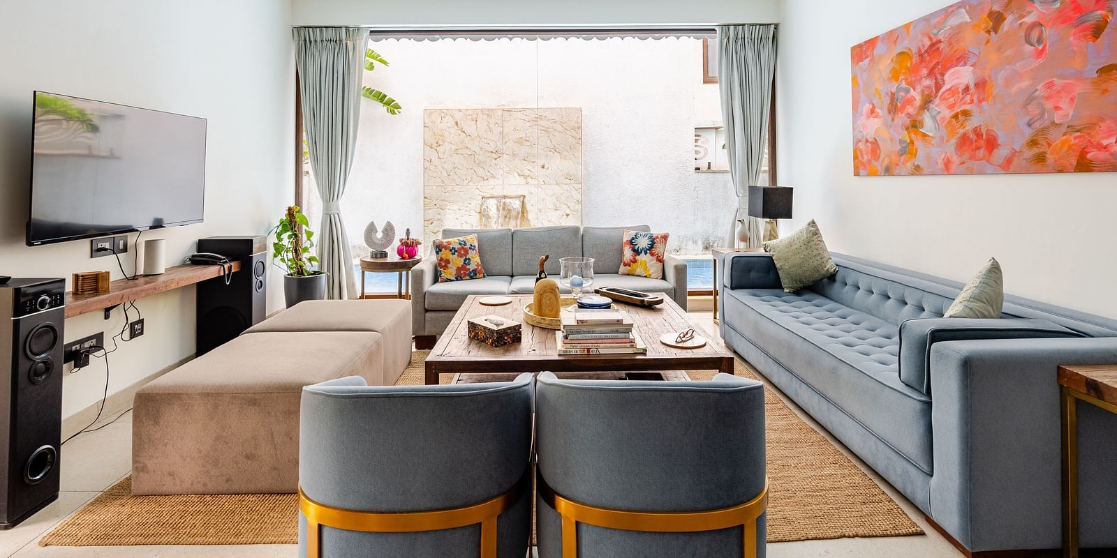 Living area at Lindsay Manor with a grey sofa set, TV, ceiling fan, abstract wall art, and an open view to an outdoor space.