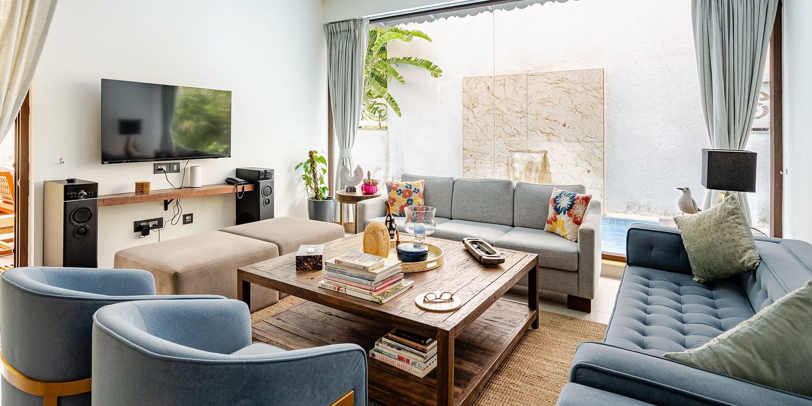 Modern living room with cosy sofas, a rustic wooden coffee table, wall-mounted TV, and large glass doors opening to a private water feature - Lindsay Manor