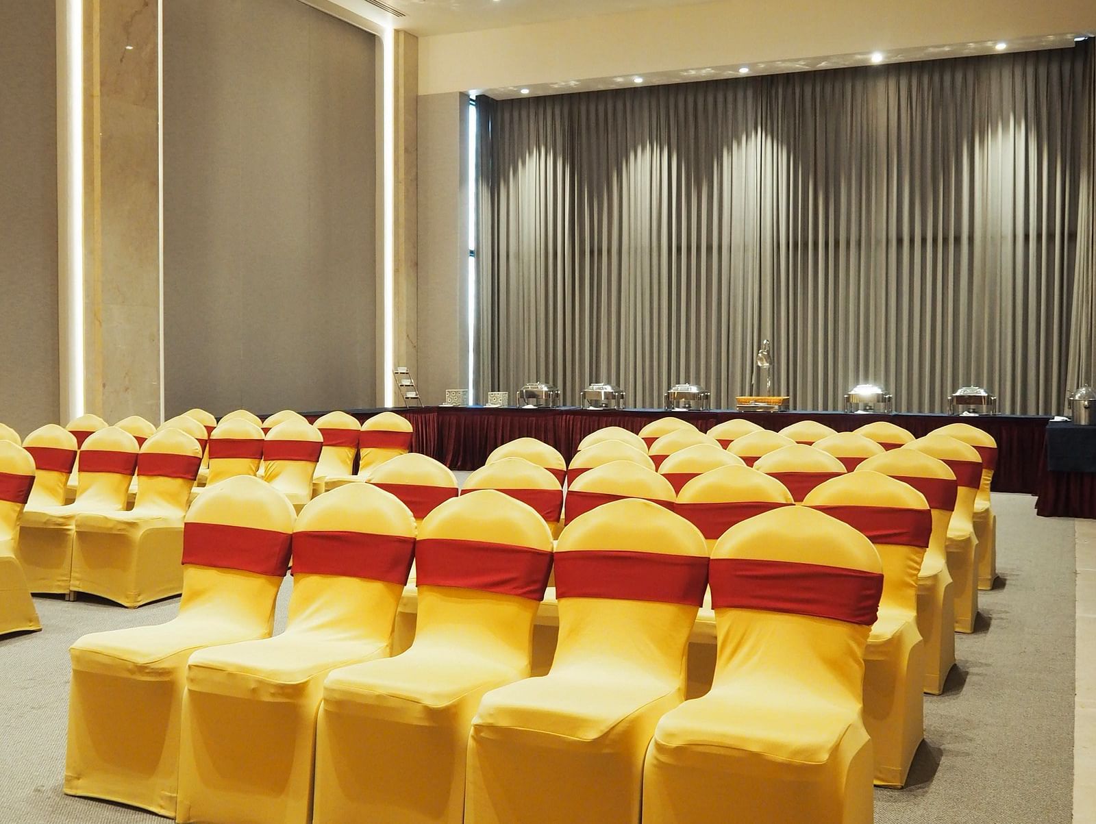 Rows of yellow chairs leading towards a curtained stage in a bright hall - Club Charholi, Pune 