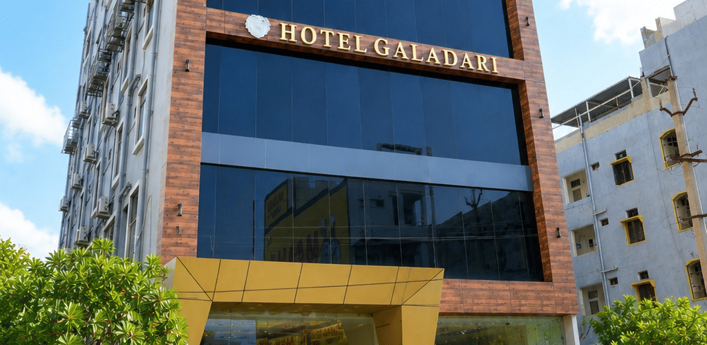 Exterior of the multistory Hotel Galadari building featuring a glass facade and landscaped entrance steps under a blue sky.