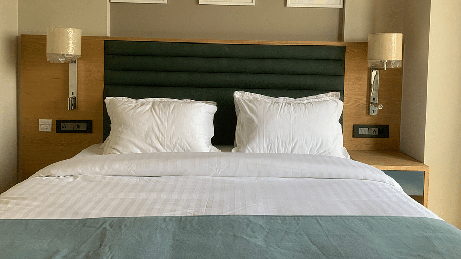 Front view of a double bed with grey besdsheet and two pillows and three white frames on the wall