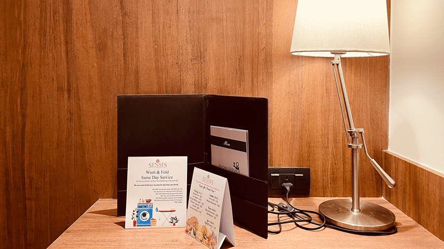 A bed side table in the Superior Room with a table lamp and a cover with several cards - Senses Hotel
