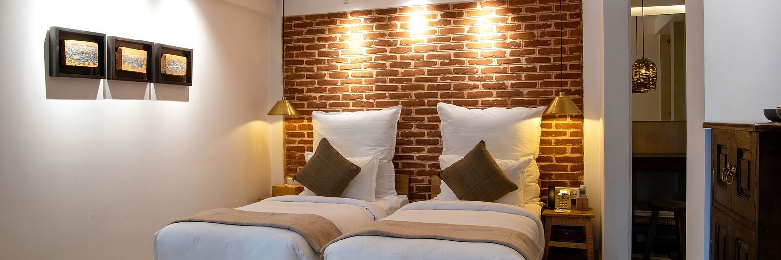 The room at The Nanee includes twin beds, bedside tables with lamps, and three pieces of artwork displayed on the wall.