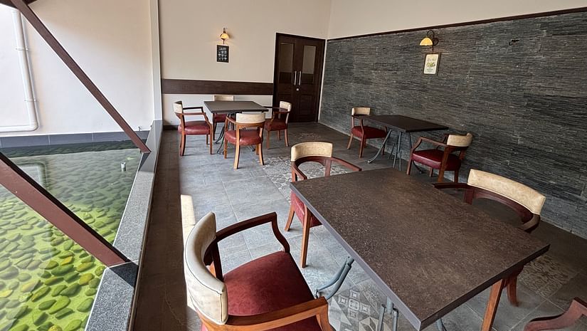 Dining area with several wooden tables and chairs, and a partial view of the roof with brown tiles at Bistro Cafe. - Still Waters, Varkala