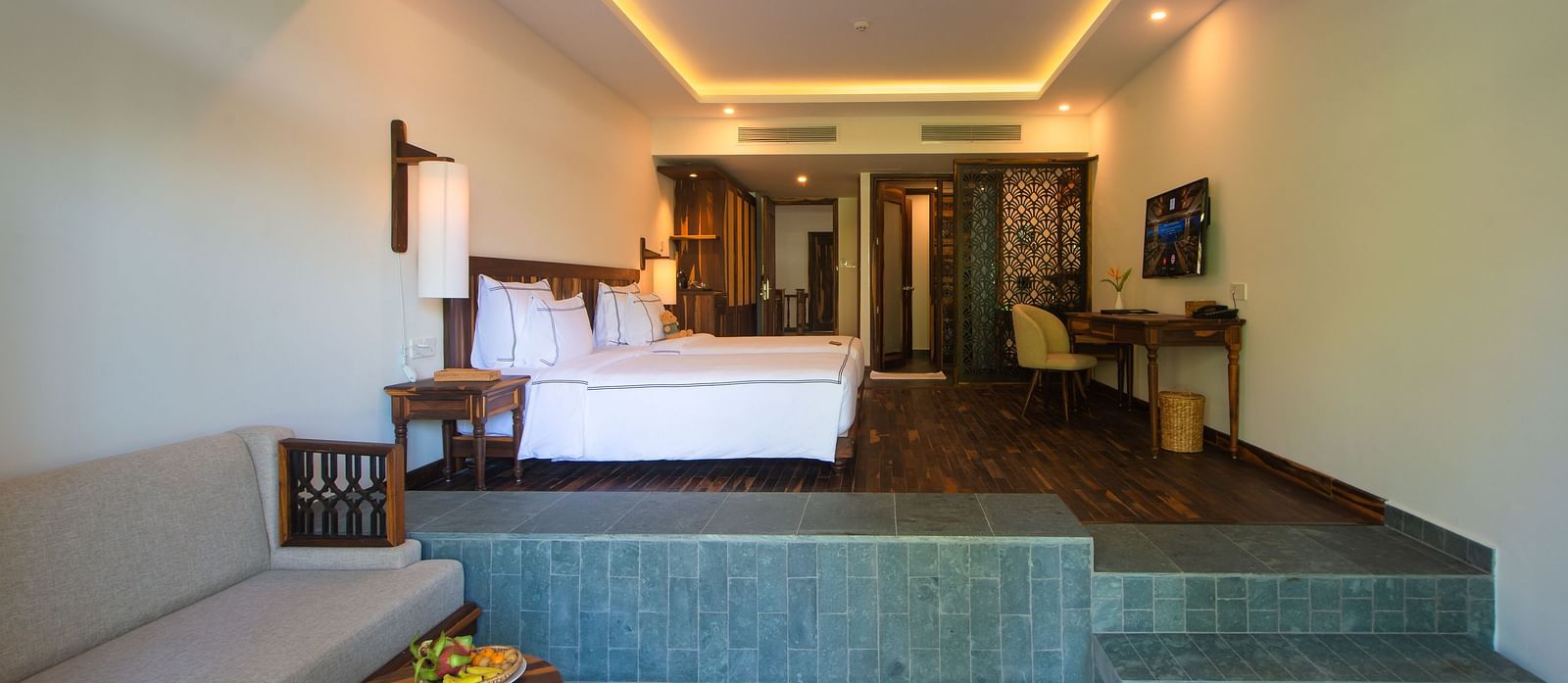 A hotel room with comfortable twin beds, furniture and a wall mounted television on a higher platform - Alibu Resort