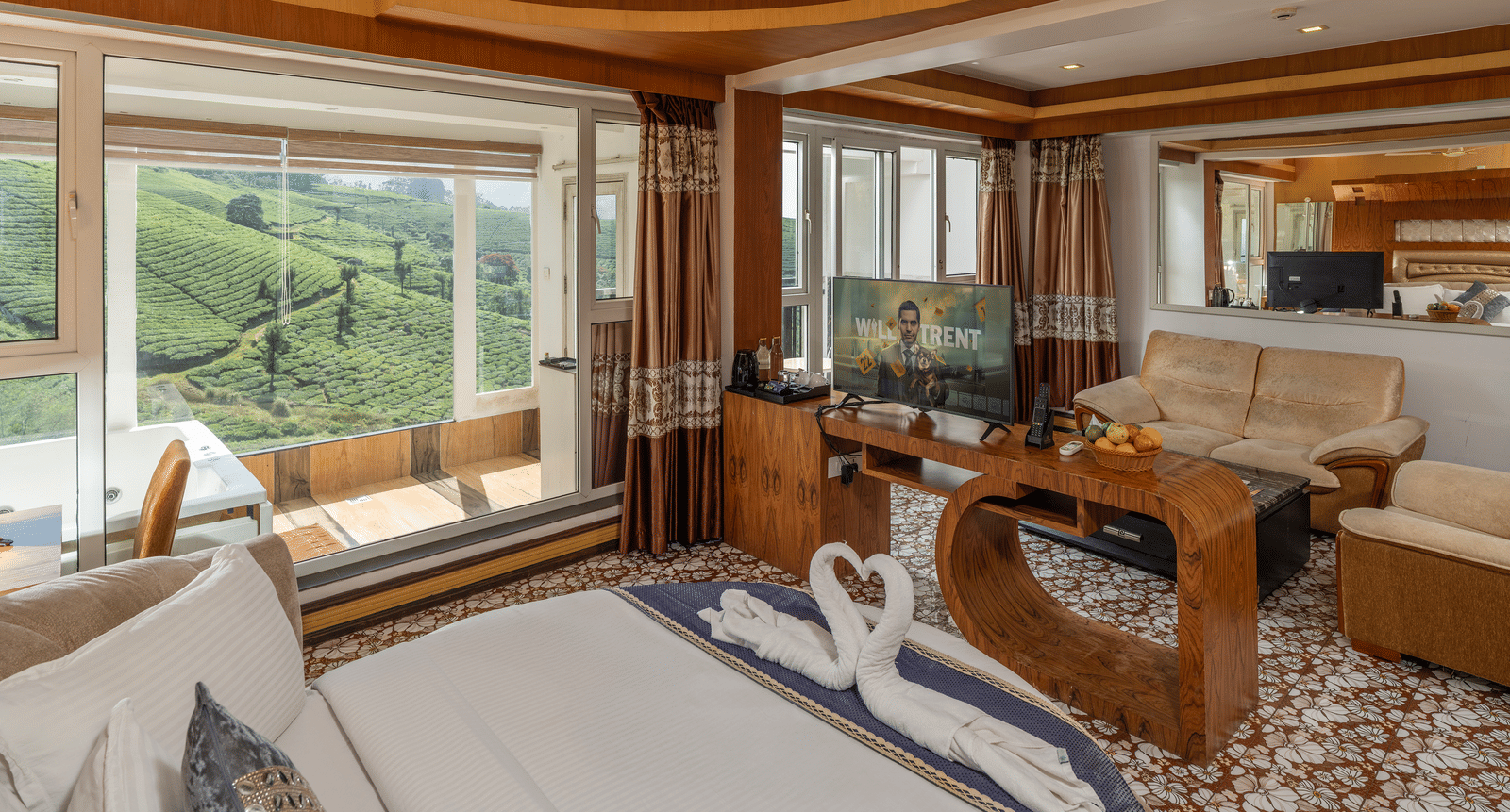 The interior of the Honey Moon Suite at Parakkat Nature Hotel and Resorts, Munnar, featuring a large bed, decorative wooden panelling, a ceiling fan, and glass windows overlooking the tea estates.