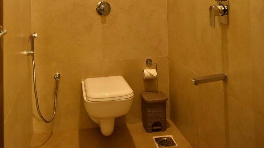 A small bathroom with a toilet, a water heater mounted on the wall, a shower, and a small window.