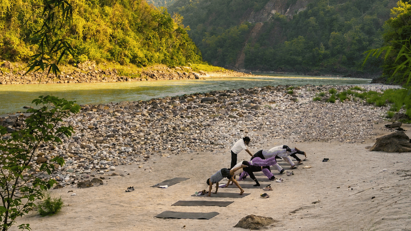 A group of people indulging into an early morning yoga session by the Ganges, with a beautiful backdrop of the hills.