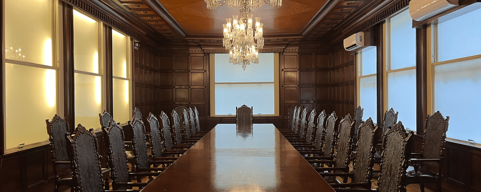 Traditional, luxurious boardroom with dark wooden panelling, a long mahogany table, and crystal chandeliers.