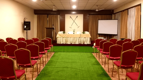 A conference room with rows of red chairs, a podium, and a projection screen.