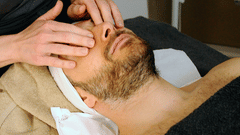 A man receiving facial massage from a masseur