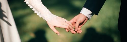 A close-up of a couple holding hands, elegantly dressed in their wedding attire.