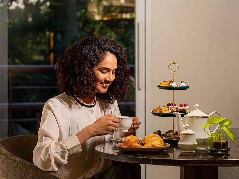 Woman in indoors with a tiered tray of pastries and tea set on the table